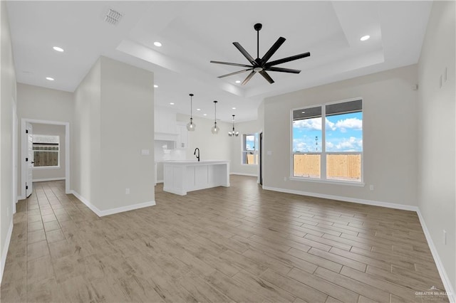 unfurnished living room featuring a tray ceiling, light wood-style flooring, visible vents, and a sink