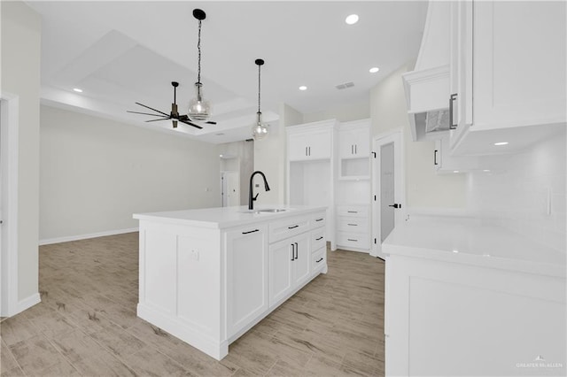 kitchen with a ceiling fan, a sink, white cabinets, light wood-style floors, and decorative light fixtures