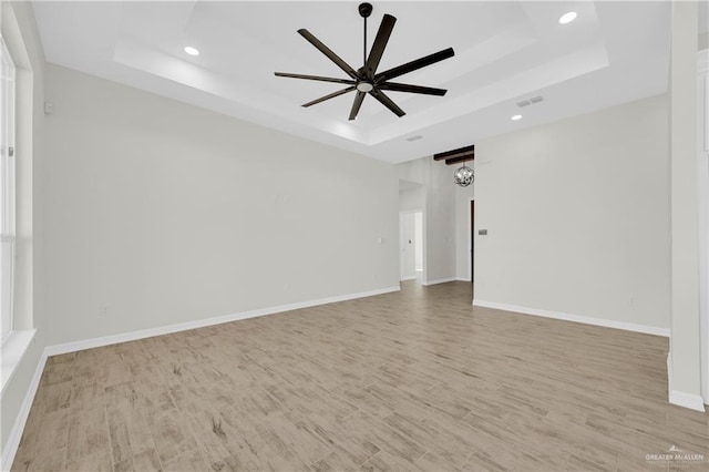 empty room featuring light wood-type flooring, visible vents, a ceiling fan, a tray ceiling, and baseboards