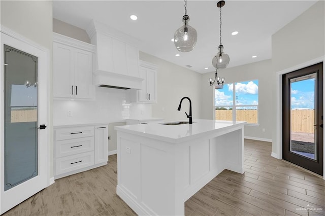 kitchen featuring light wood-style flooring, an island with sink, a sink, white cabinetry, and decorative light fixtures