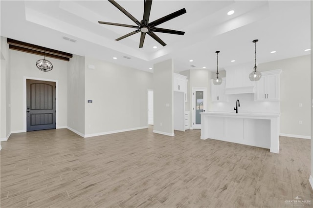 unfurnished living room with recessed lighting, a tray ceiling, light wood-style floors, and visible vents