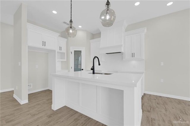 kitchen featuring light wood-type flooring, a center island with sink, a sink, white cabinetry, and hanging light fixtures