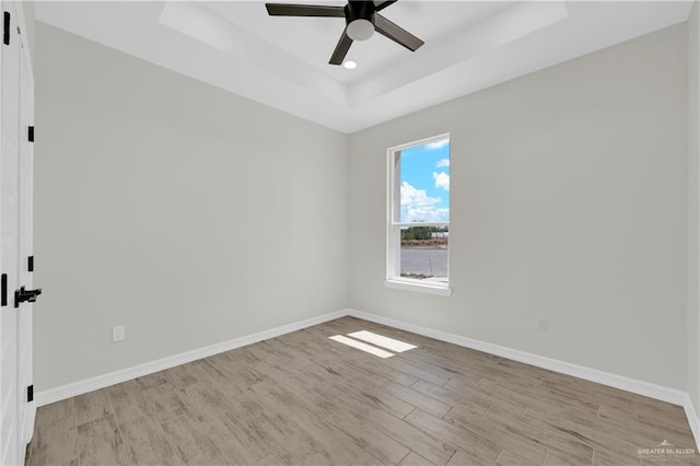 empty room featuring light wood-type flooring, baseboards, a raised ceiling, and a ceiling fan