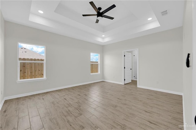 empty room featuring a tray ceiling, baseboards, light wood-style floors, and a ceiling fan