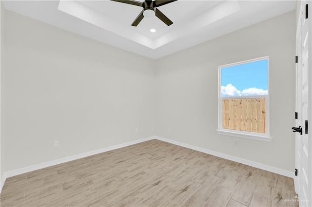 spare room featuring a raised ceiling, light wood-style floors, baseboards, and ceiling fan