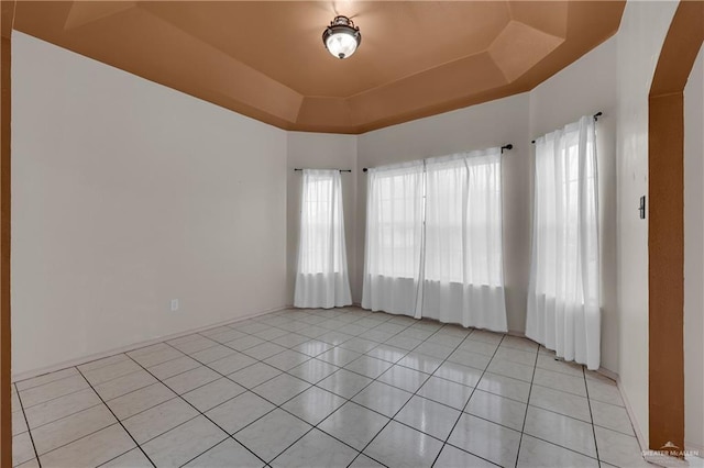 tiled empty room with plenty of natural light and a raised ceiling