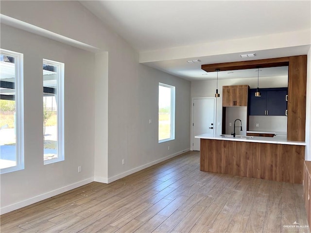 kitchen with sink, decorative light fixtures, vaulted ceiling, kitchen peninsula, and light wood-type flooring