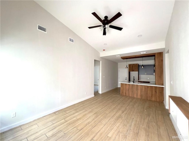 unfurnished living room featuring sink, vaulted ceiling, ceiling fan, and light wood-type flooring