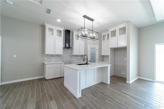 kitchen featuring wall chimney exhaust hood, a sink, a chandelier, tasteful backsplash, and wood finished floors