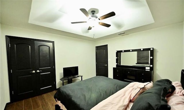 bedroom with ceiling fan, a raised ceiling, and dark wood-type flooring