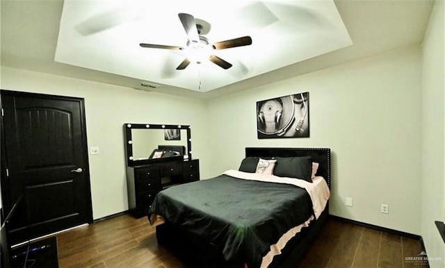 bedroom with a raised ceiling, ceiling fan, and dark wood-type flooring