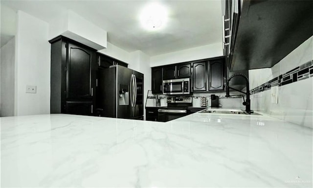 kitchen with stainless steel appliances, light stone counters, and sink