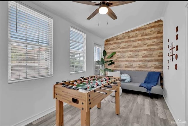 recreation room with wooden walls, ceiling fan, wood-type flooring, and lofted ceiling