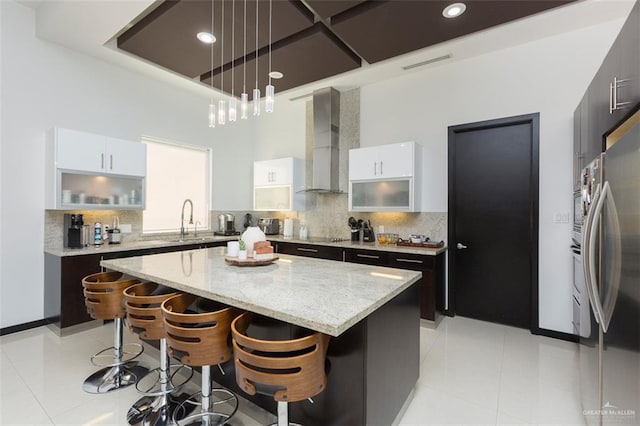 kitchen featuring stainless steel refrigerator, a center island, wall chimney range hood, tasteful backsplash, and white cabinets