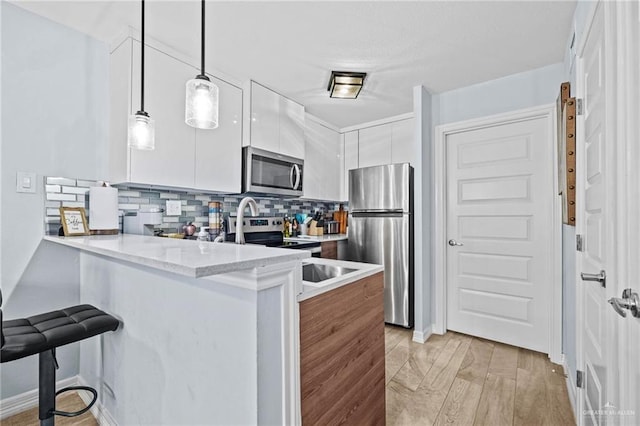 kitchen featuring a breakfast bar, white cabinets, decorative light fixtures, light stone counters, and stainless steel appliances