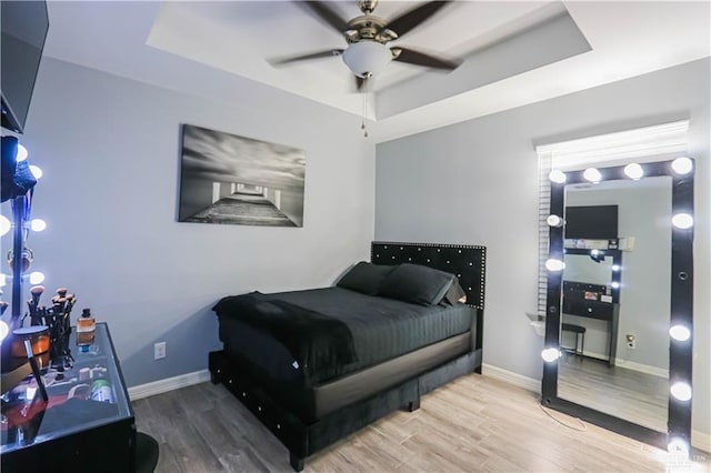 bedroom with hardwood / wood-style floors, ceiling fan, and a tray ceiling