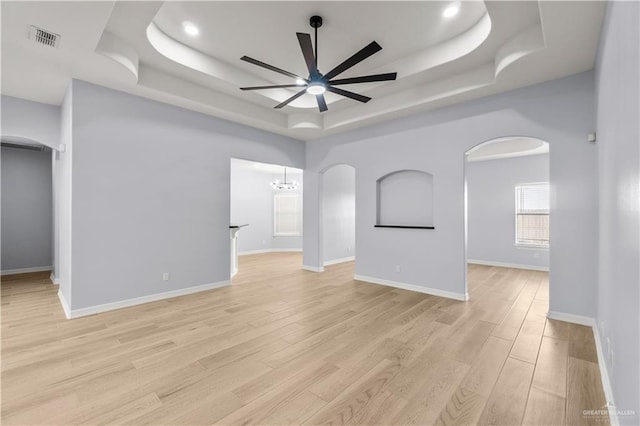 unfurnished room with a raised ceiling, ceiling fan with notable chandelier, and light hardwood / wood-style flooring