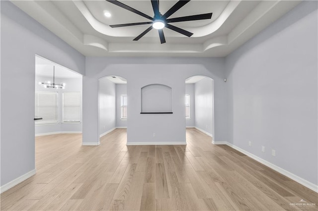 unfurnished living room with a tray ceiling, ceiling fan with notable chandelier, and light wood-type flooring