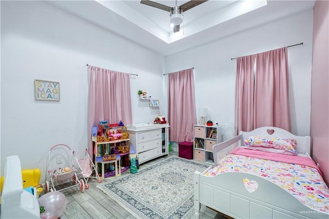 bedroom featuring a raised ceiling, ceiling fan, and wood finished floors