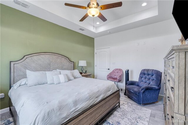 bedroom featuring light wood-type flooring, visible vents, a raised ceiling, and recessed lighting