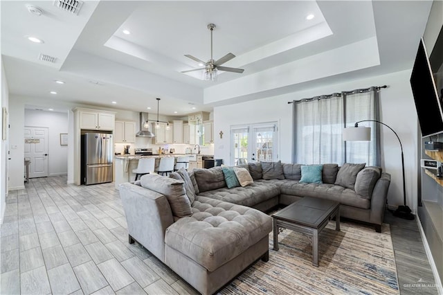 living area featuring visible vents, light wood-style flooring, a raised ceiling, and ceiling fan