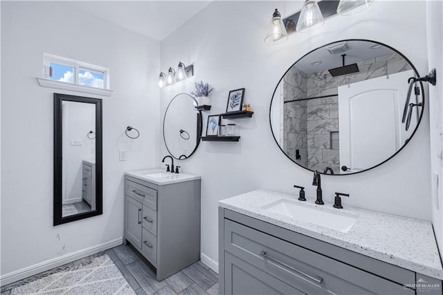 full bath featuring a sink, tiled shower, baseboards, and two vanities