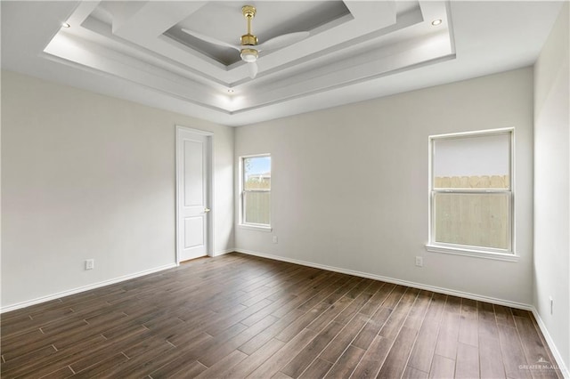 unfurnished room with a tray ceiling, ceiling fan, and dark wood-type flooring