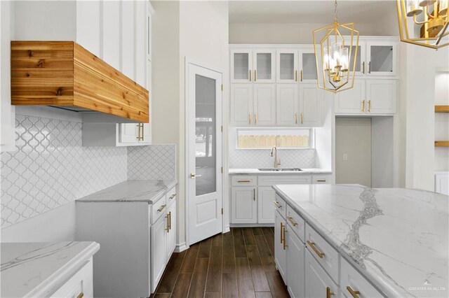 kitchen with sink, light stone counters, dark hardwood / wood-style floors, decorative light fixtures, and white cabinets