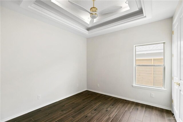 empty room featuring a raised ceiling, ceiling fan, and dark wood-type flooring