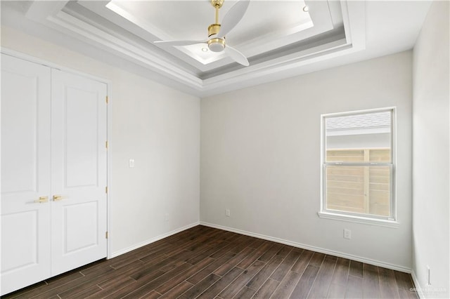 unfurnished room with ceiling fan, a raised ceiling, and dark wood-type flooring