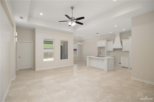 unfurnished living room with ceiling fan with notable chandelier, a raised ceiling, and sink