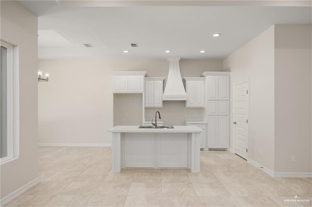 kitchen featuring premium range hood, sink, white cabinets, a chandelier, and an island with sink