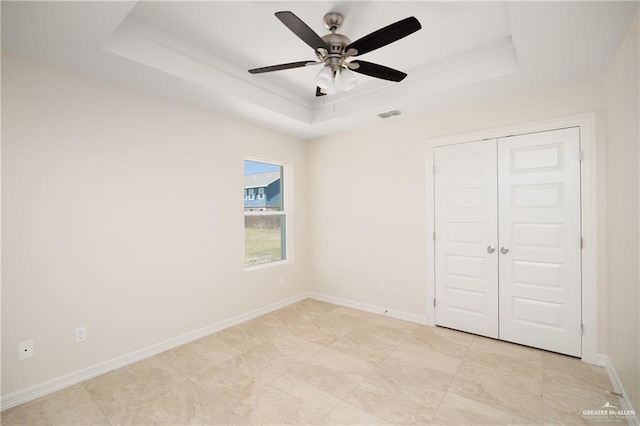 unfurnished bedroom with a tray ceiling, ceiling fan, and a closet