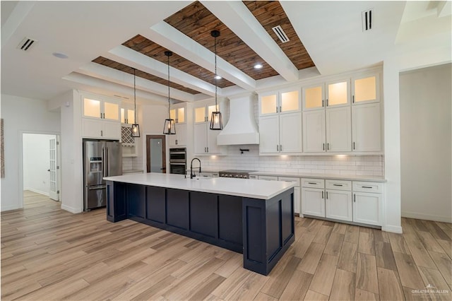 kitchen featuring white cabinets, beamed ceiling, stainless steel appliances, and custom range hood