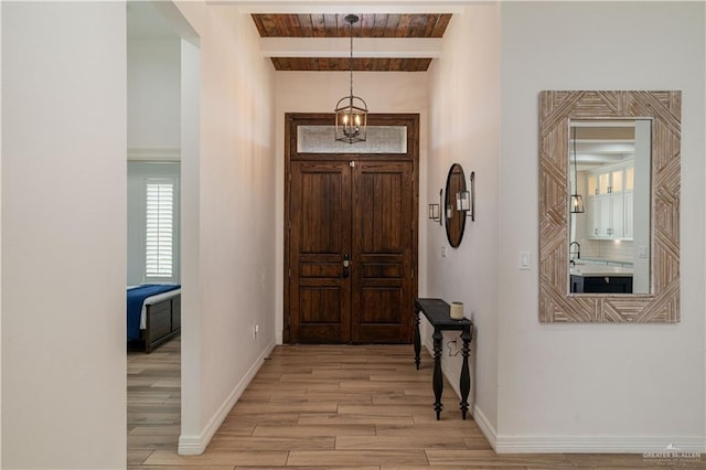 foyer with light hardwood / wood-style flooring, beamed ceiling, an inviting chandelier, and sink