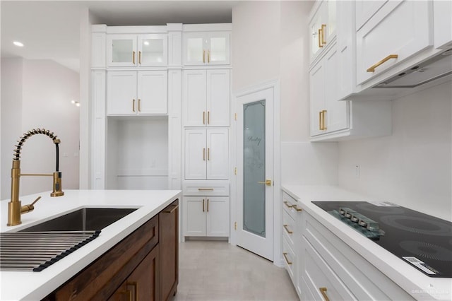 kitchen featuring black electric stovetop, light countertops, glass insert cabinets, white cabinetry, and a sink