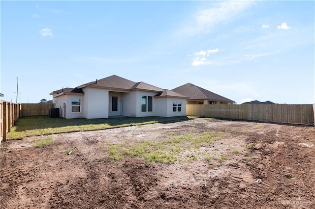 back of house with stucco siding, a fenced backyard, central AC, and a yard