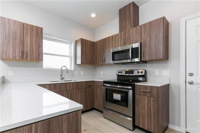 kitchen featuring light stone countertops, light wood-type flooring, sink, and appliances with stainless steel finishes