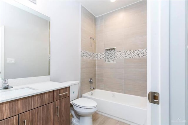 full bathroom with hardwood / wood-style floors, vanity, tiled shower / bath combo, and toilet