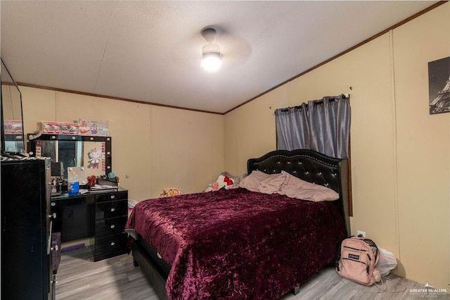 bedroom with ornamental molding, light wood finished floors, vaulted ceiling, and a textured ceiling