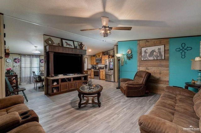 living area featuring vaulted ceiling, ceiling fan, a textured ceiling, and light wood-style flooring