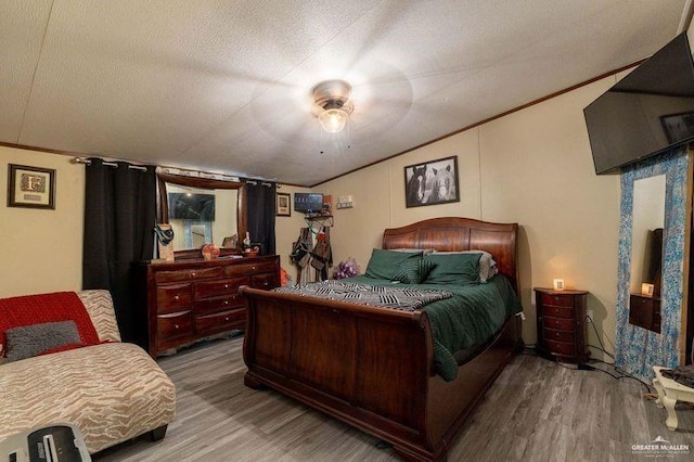 bedroom featuring ornamental molding, lofted ceiling, a textured ceiling, and wood finished floors