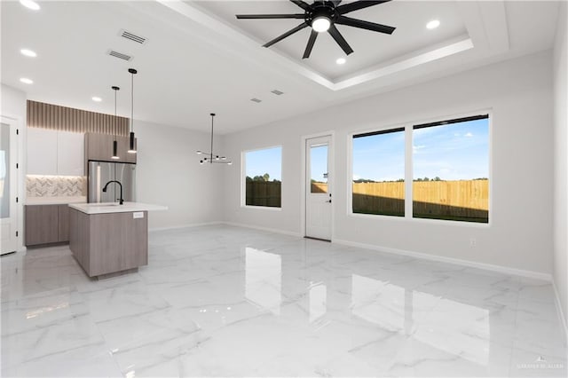 unfurnished living room with ceiling fan with notable chandelier and a raised ceiling