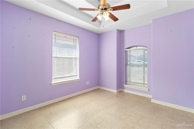 tiled spare room featuring ceiling fan, plenty of natural light, and a tray ceiling