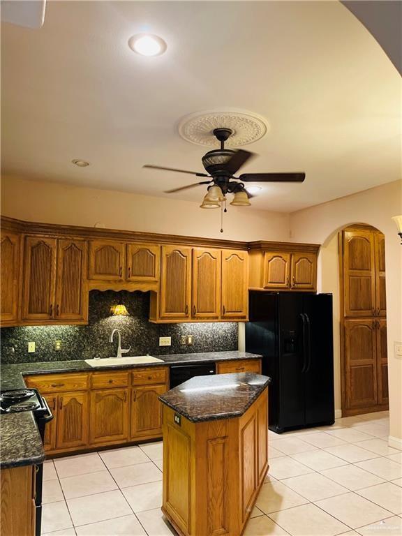 kitchen featuring arched walkways, black appliances, a sink, a ceiling fan, and dark stone counters