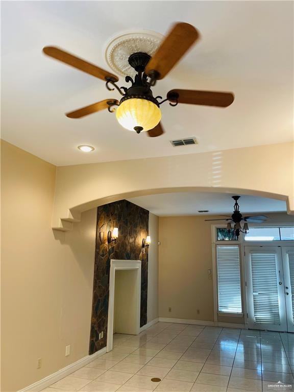 unfurnished living room with ceiling fan, arched walkways, baseboards, and light tile patterned flooring