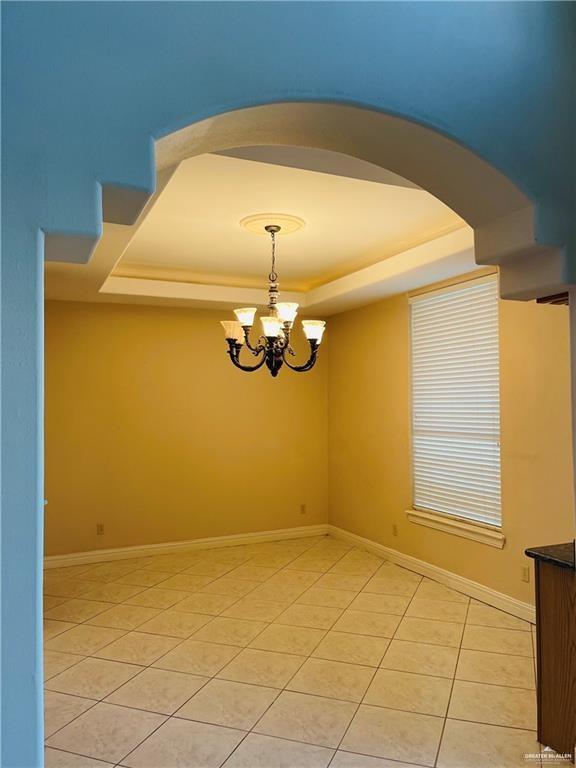 unfurnished room featuring a tray ceiling, light tile patterned flooring, a chandelier, arched walkways, and baseboards
