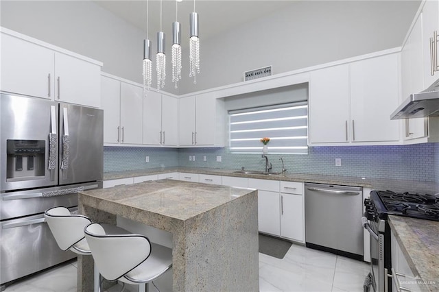 kitchen with appliances with stainless steel finishes, a breakfast bar, a sink, marble finish floor, and decorative backsplash