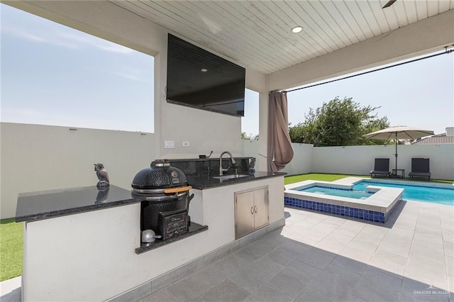 view of patio / terrace featuring a fenced backyard, a pool with connected hot tub, a sink, and an outdoor kitchen