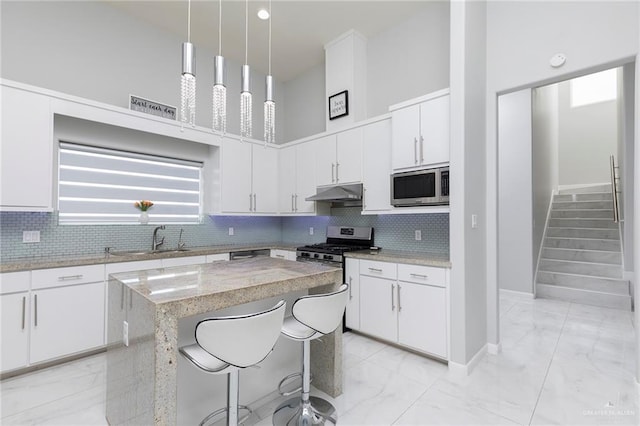kitchen featuring white cabinets, a sink, marble finish floor, stainless steel appliances, and under cabinet range hood